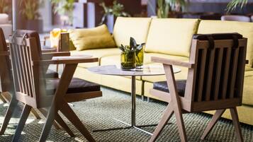 Uma sala de estar moderna com um sofá amarelo, cadeiras de madeira, uma mesa redonda pequena e um vaso com plantas verdes.