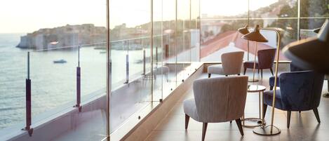 Un intérieur moderne avec vue sur la mer, agrémenté d’une balustrade en verre, de chaises contemporaines et d’un lampadaire.
