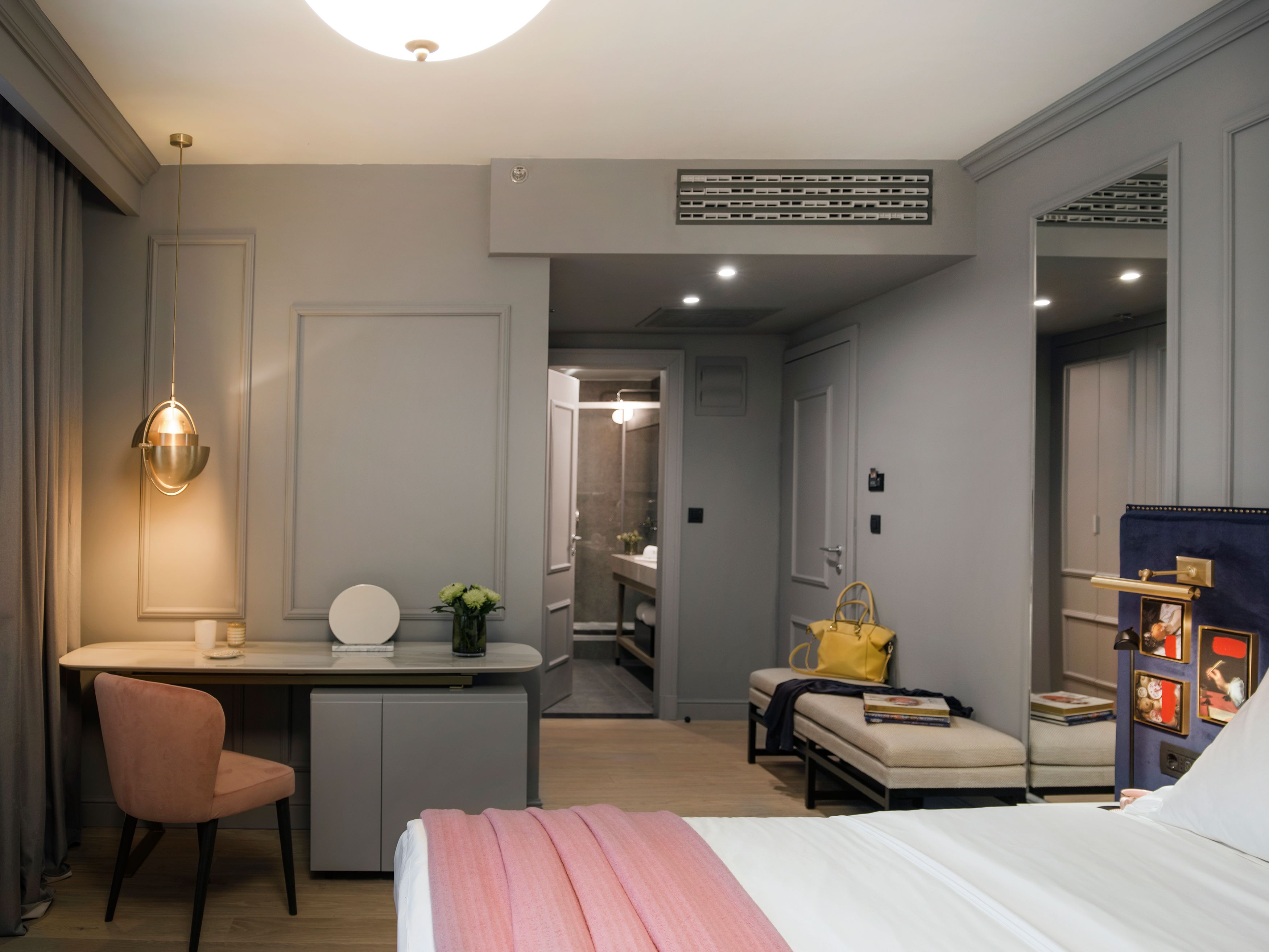 A modern hotel room with a bed, a desk, a chair, a sofa, and a small table with a handbag.