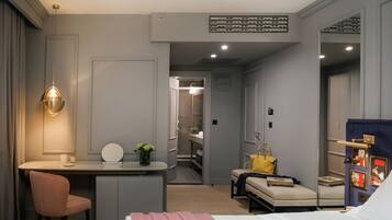 A modern hotel room with a bed, a desk, a chair, a sofa, and a small table with a handbag.