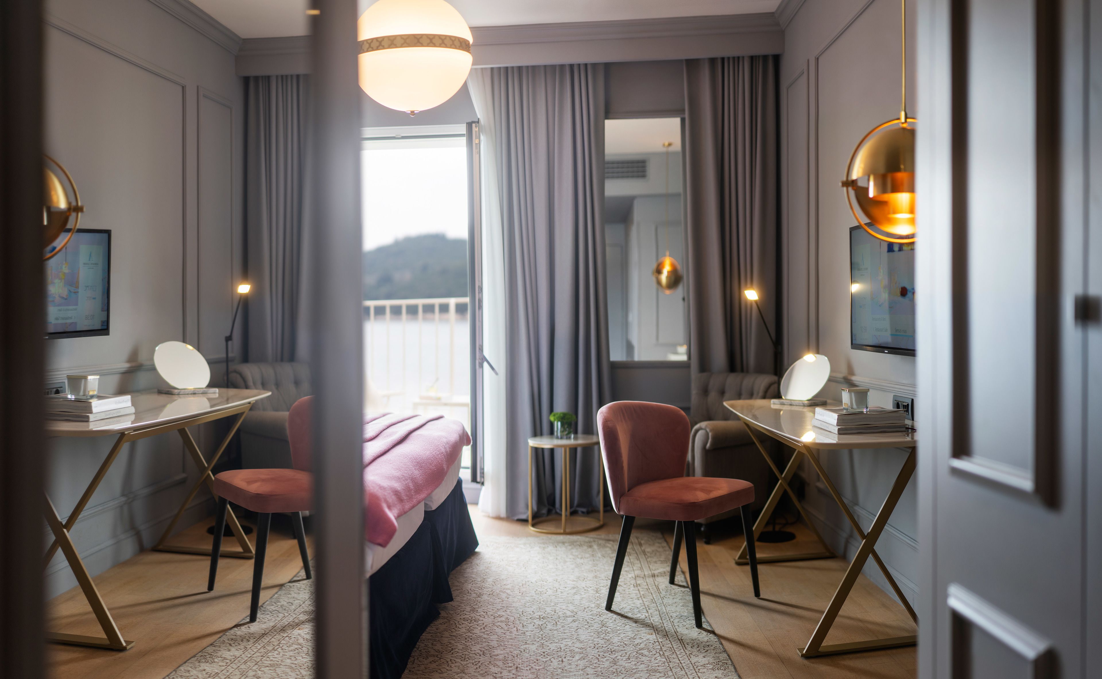 A hotel room with a bed, two desks, two chairs, a small table, and a view of the outdoors.
