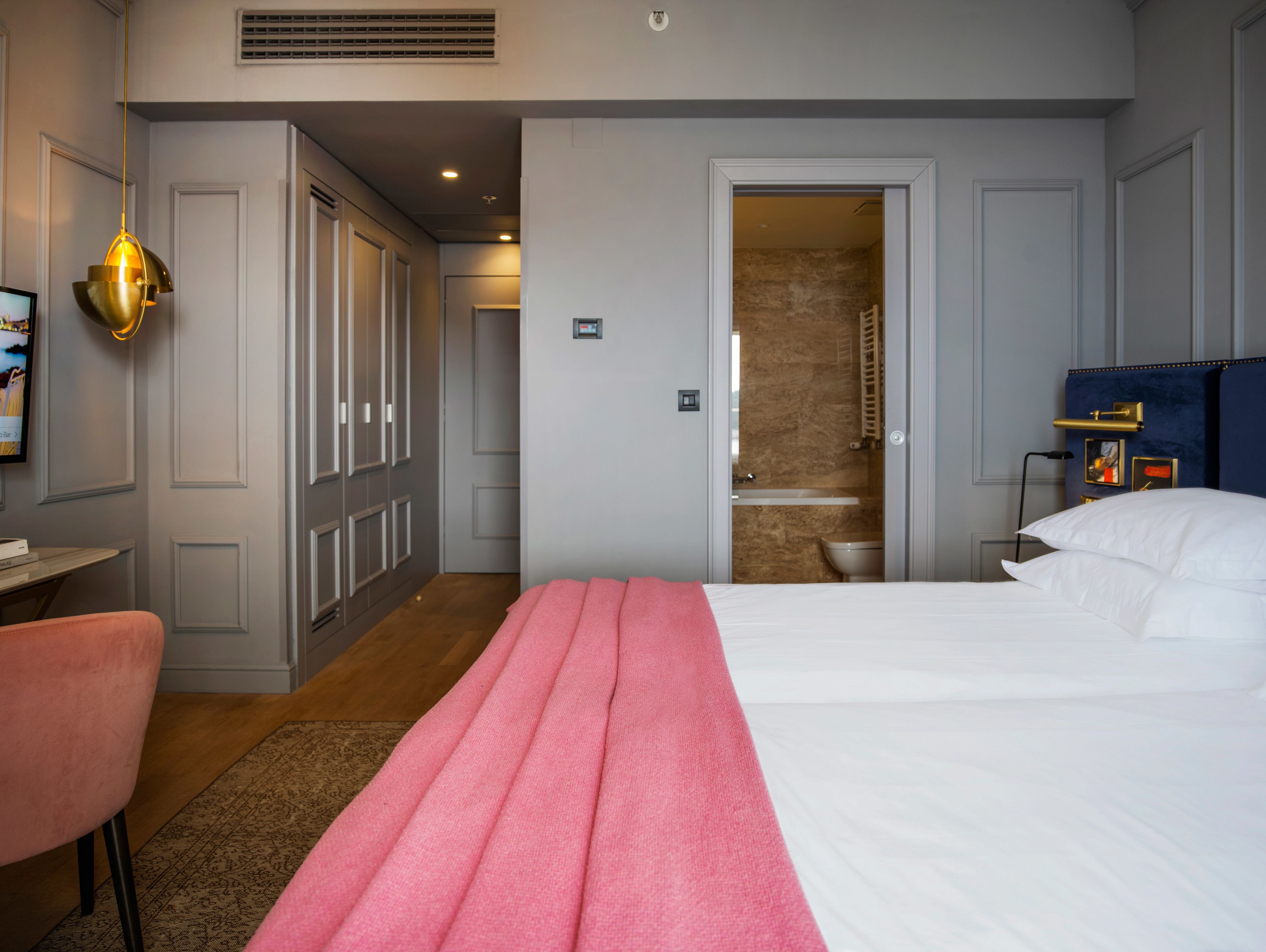 Une chambre d’hôtel avec un lit, un bureau, une chaise, une armoire et une salle de bain visible à travers une porte ouverte.