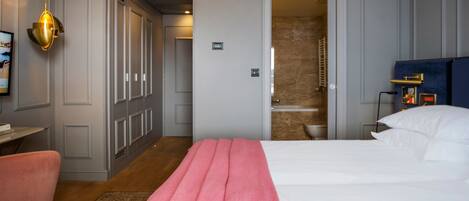 Une chambre d’hôtel avec un lit, un bureau, une chaise, une armoire et une salle de bain visible à travers une porte ouverte.