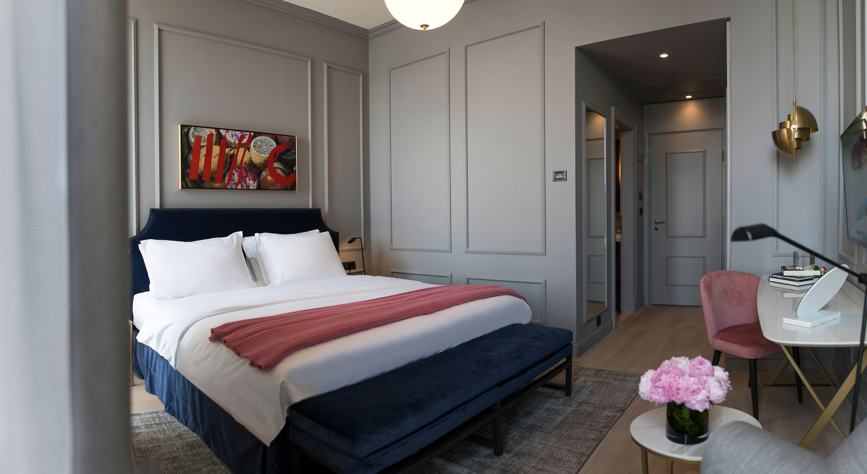 A modern hotel room with a large bed, a desk with a chair, and a painting on the wall.