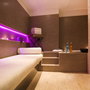A modern bathroom with a wooden bench, a shelf with folded towels, and a counter with bottles.