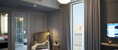 A hotel room with a bed, a chair, a desk, a TV, and a window with curtains.