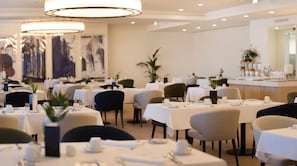 A well-lit dining area with round tables, chairs, and a bar area in the background.