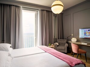 Habitación de hotel con cama, escritorio, silla, televisor y vista al mar.