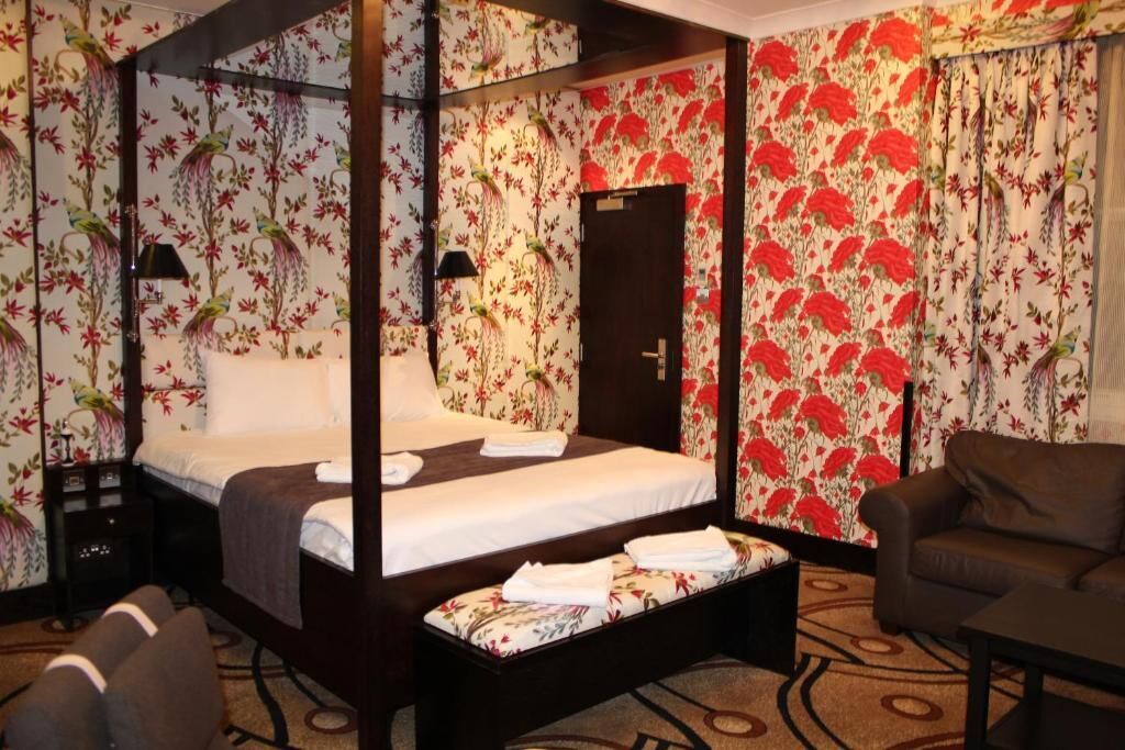Uma cama de dossel com papel de parede floral, uma mesinha de cabeceira, uma cadeira e uma pequena mesa.