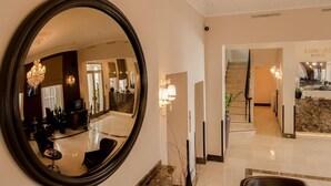 A hotel lobby with a reception desk, a chandelier, and a large mirror reflecting the interior. - Edward Hotel Paddington (London)