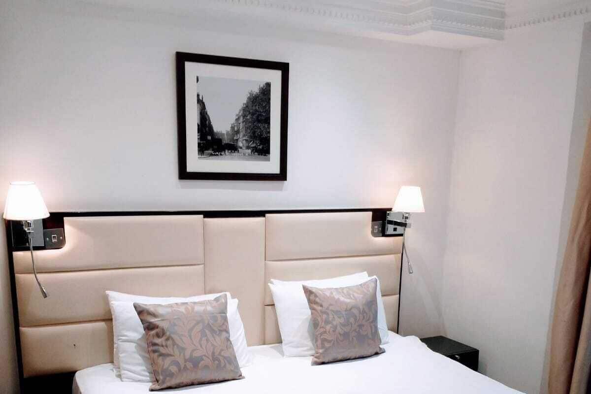 A hotel room with a large bed, two bedside lamps, a framed picture on the wall, and a neatly made bed with a towel.