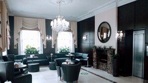 A lobby with a chandelier, sofas, a fireplace, and a mirror. - Edward Hotel Paddington (London)
