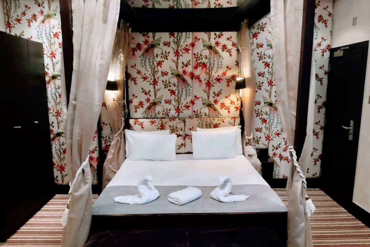 A hotel room with a bed, floral wallpaper, and a striped carpet.