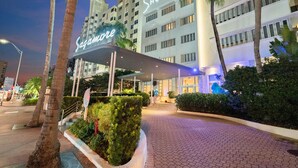 A hotel entrance with a covered walkway, palm trees, and a sign reading "Sagamore."
