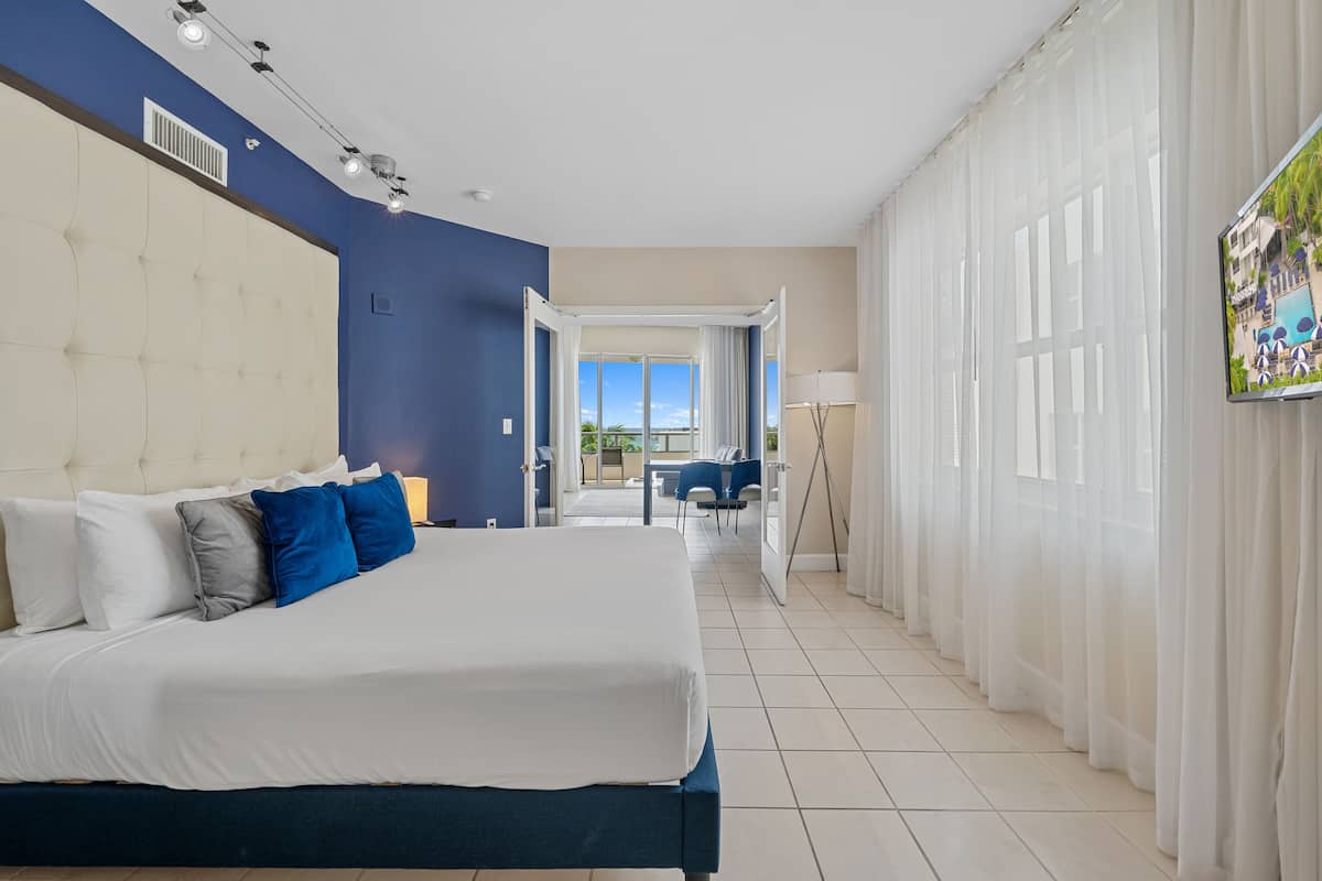 A hotel room with a large bed, a TV, and a view of the outdoors.