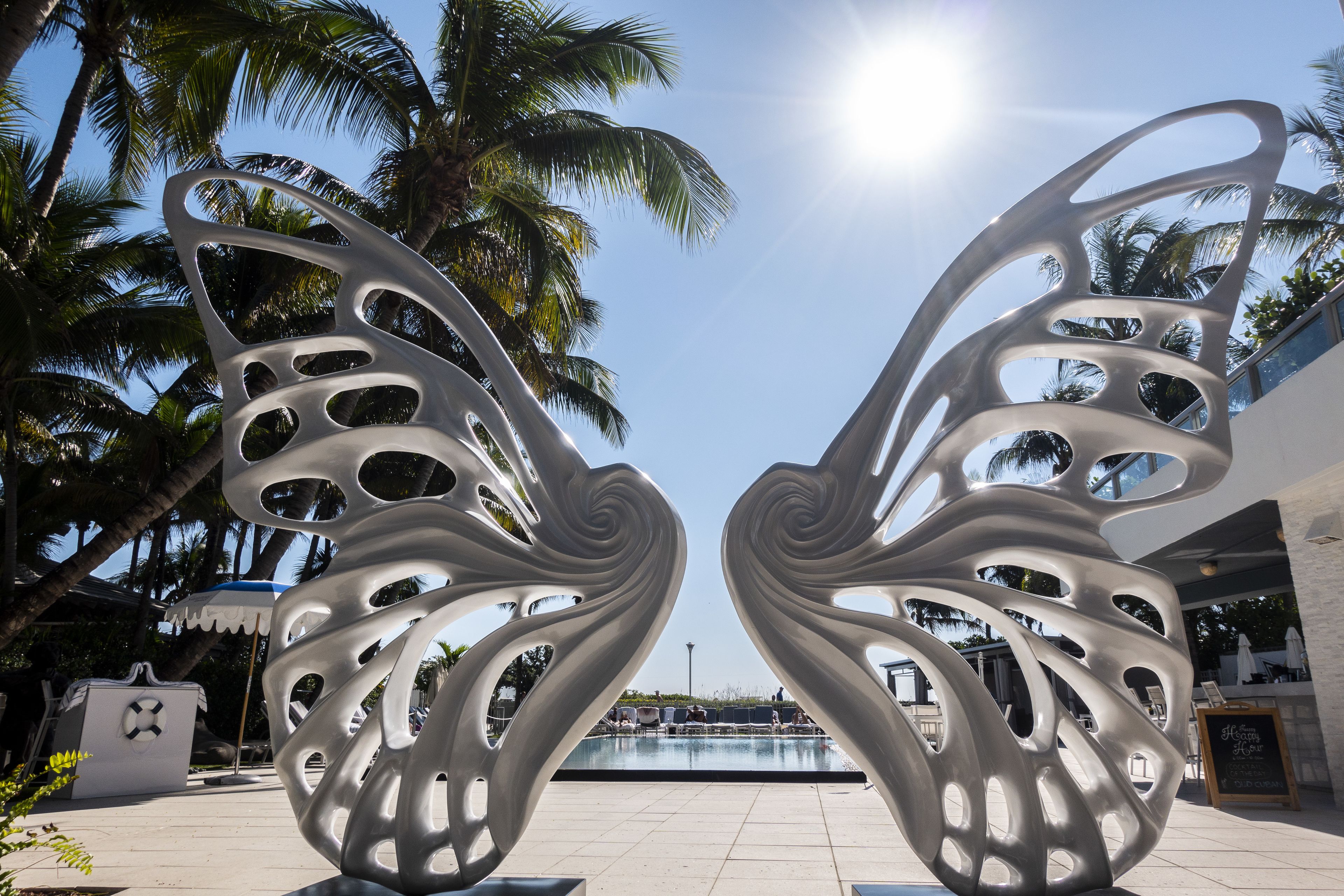 A modern outdoor area with a pool, palm trees, and a unique metal sculpture.