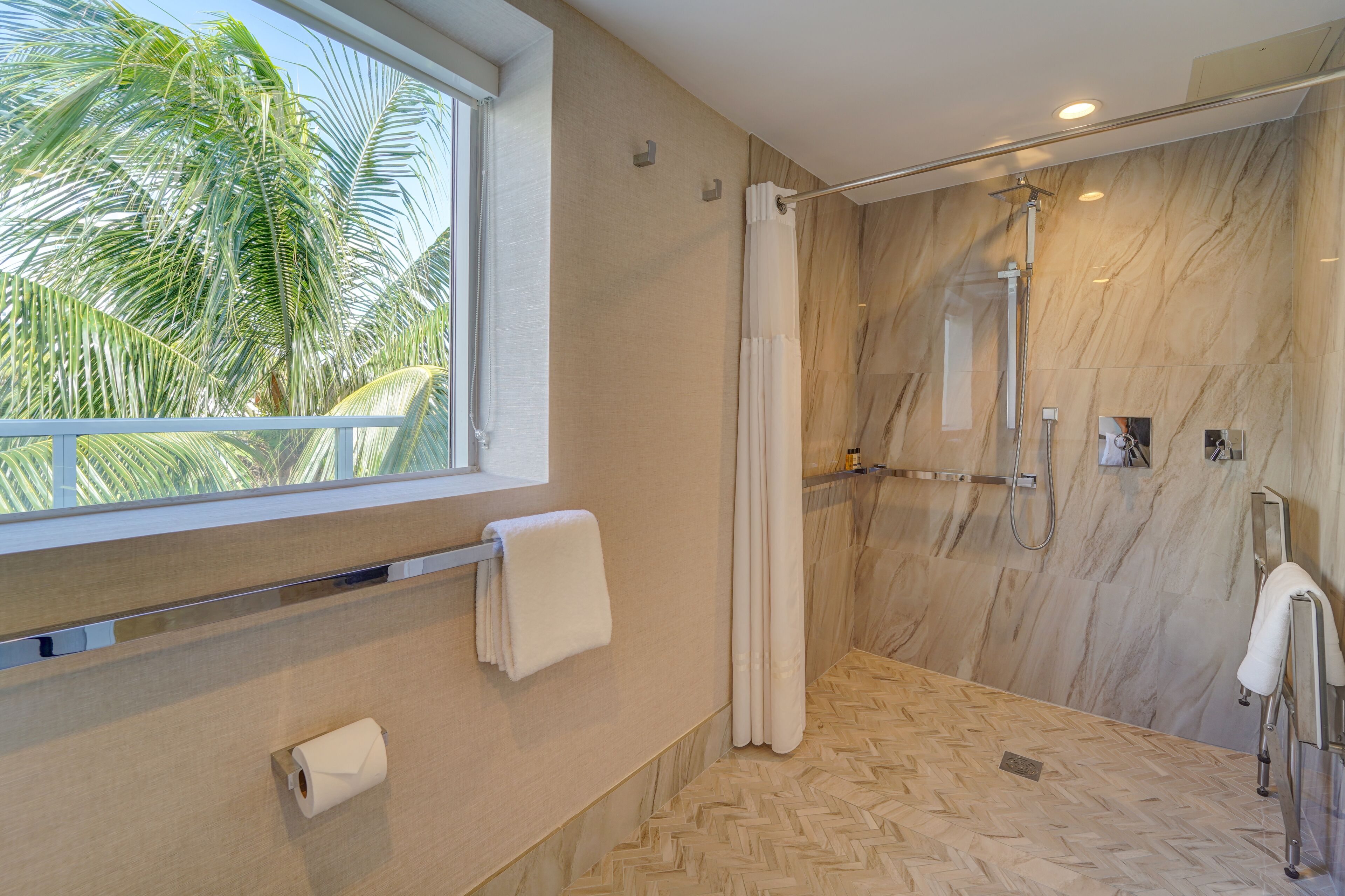 Une salle de bain moderne avec une douche, une fenêtre donnant sur des palmiers et un porte-serviettes.
