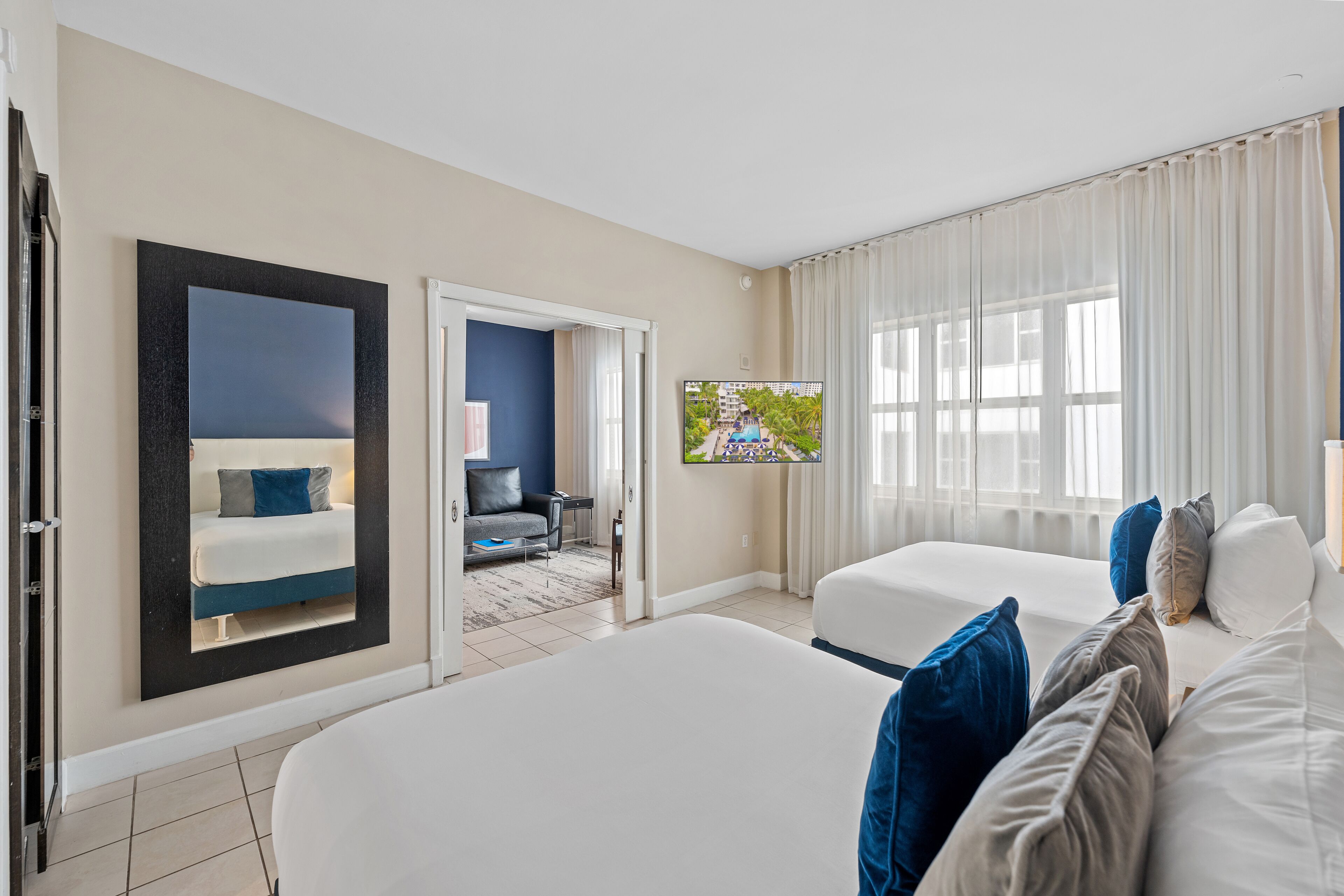 A hotel room with two beds, a large mirror, a TV, and a view of a pool.