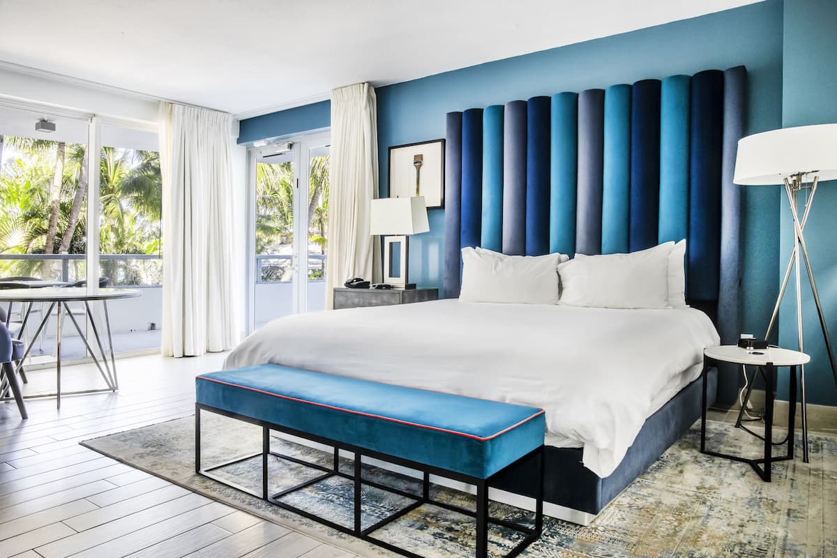A modern bedroom with a large bed, a bench, a bedside table, and a floor lamp.