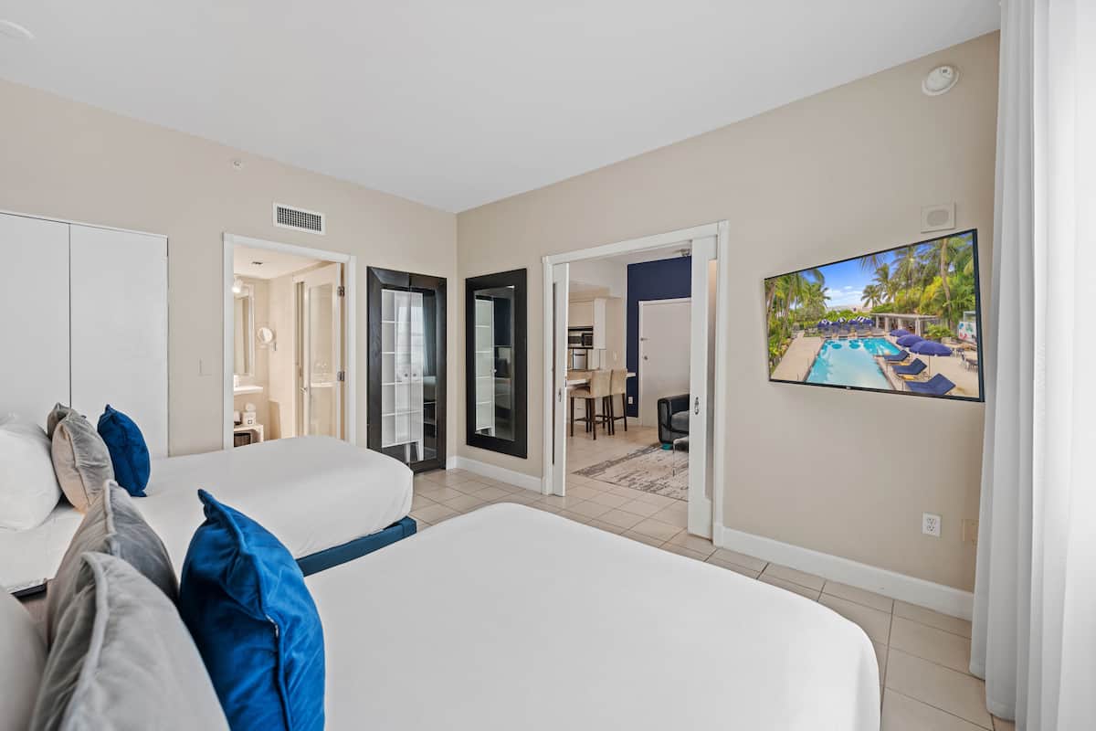 A hotel room with two beds, a TV displaying a pool, and a view of a pool area through an open door.