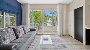 A modern living room with a grey sofa, a white coffee table, and a view of a balcony with plants.