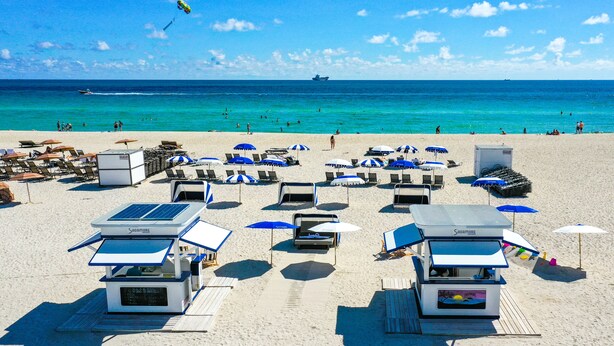 A beach with sun loungers, umbrellas, and a lifeguard stand.
