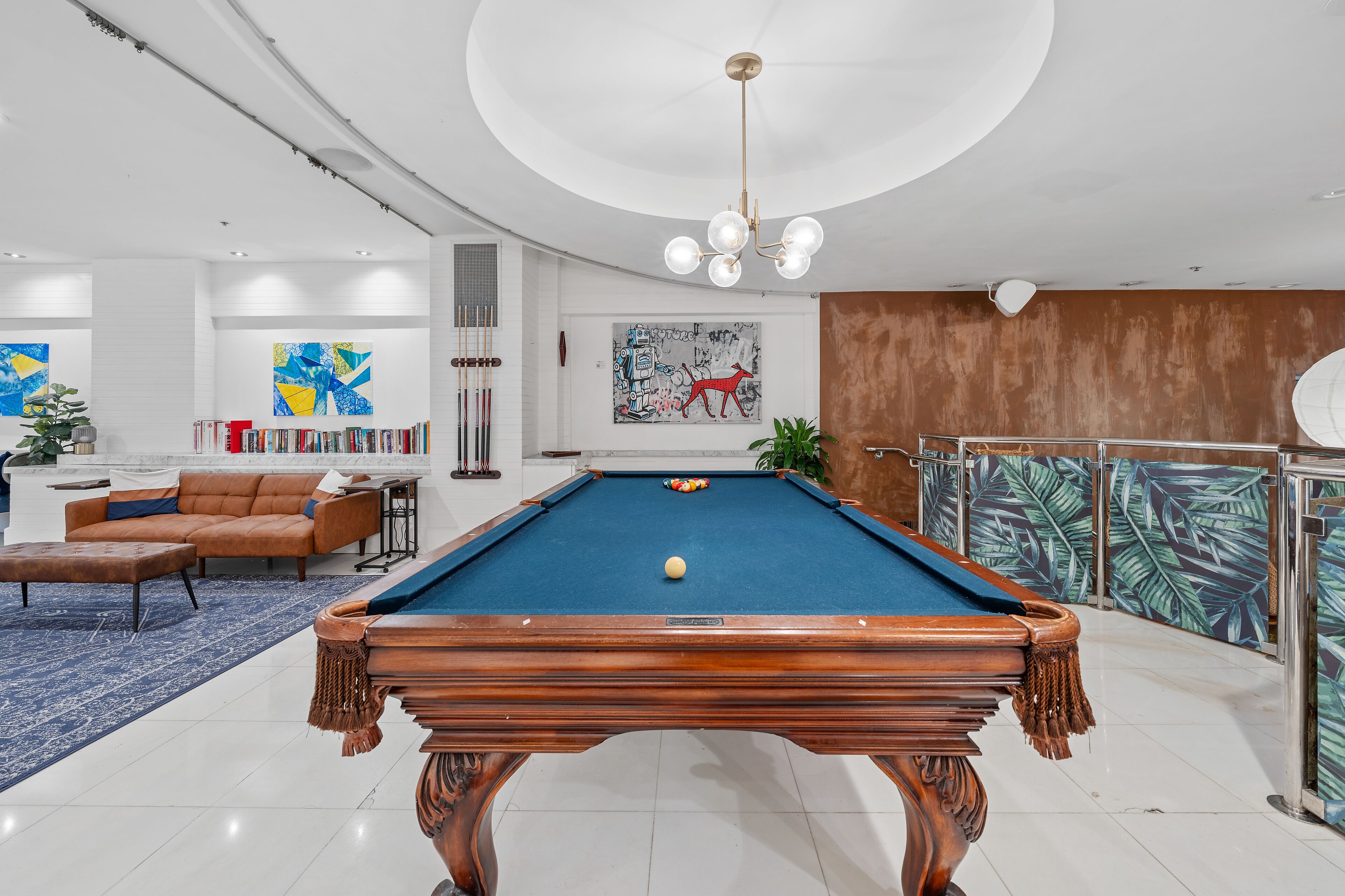 A pool table in a modern living room with a sofa, bookshelves, and artwork.