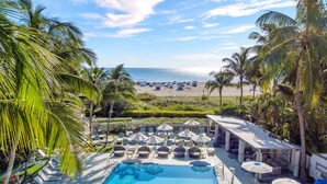 A pool area with lounge chairs and umbrellas, a beach view, and palm trees.