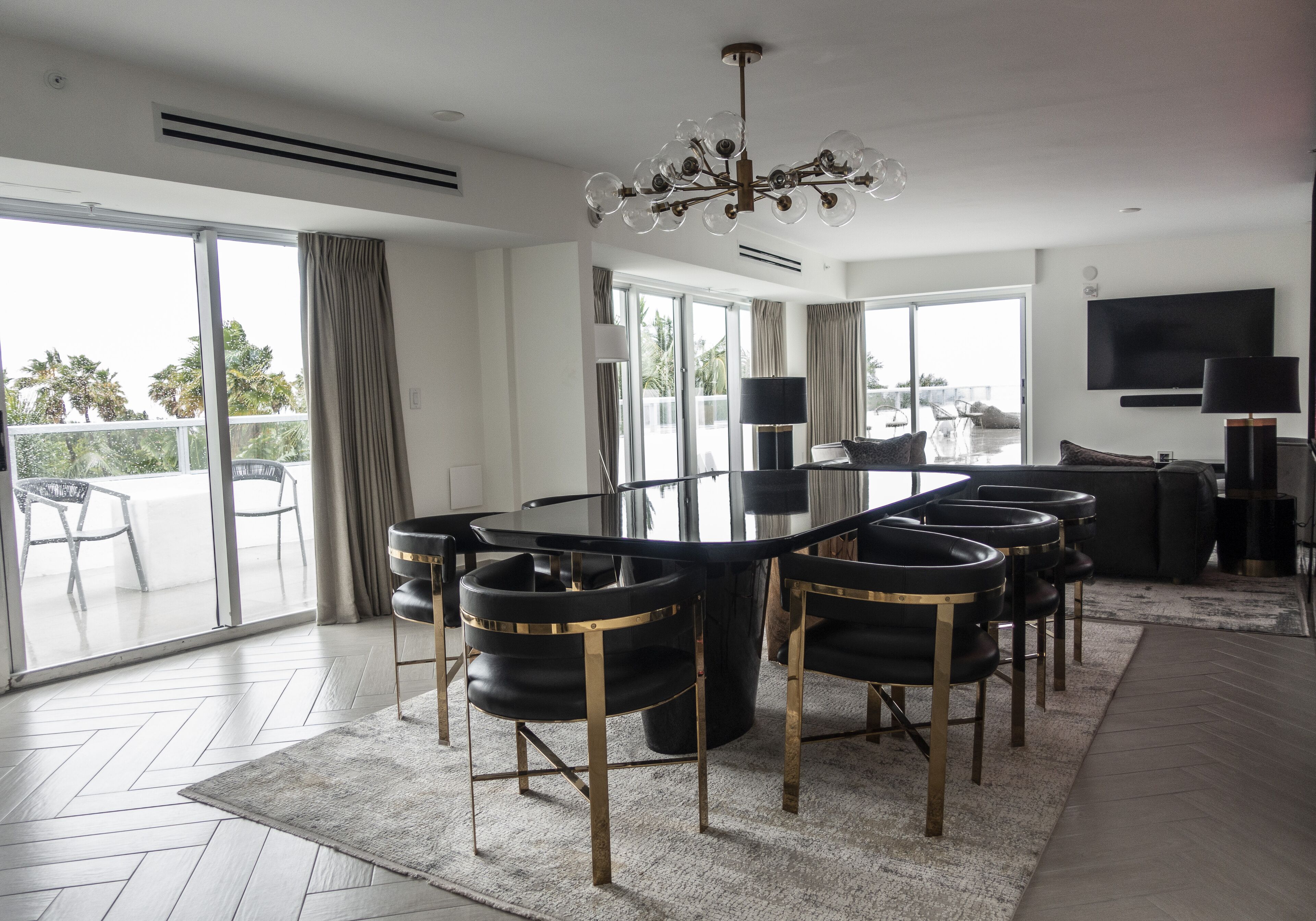 Een moderne eethoek met een tafel met glazen blad, zwarte stoelen met gouden accenten en een kroonluchter.