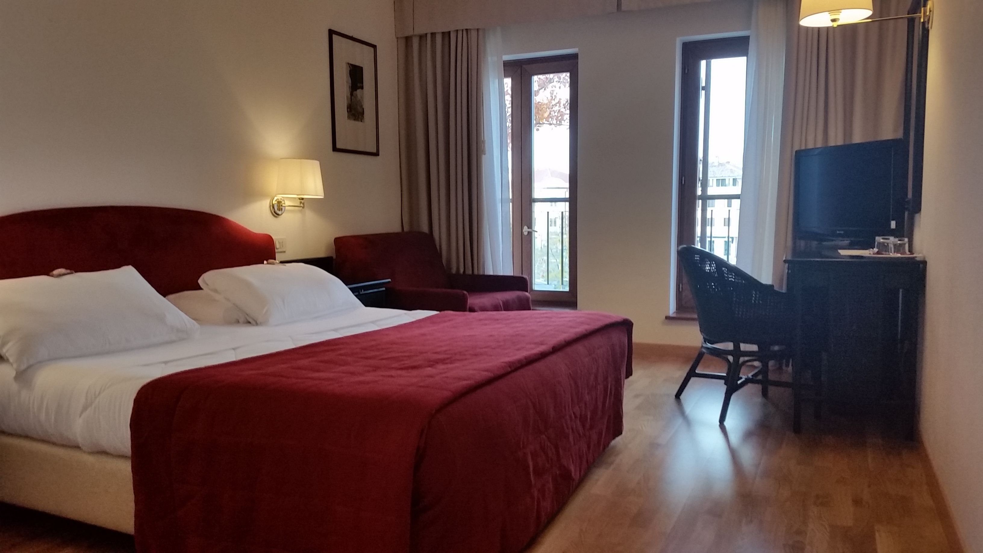 Habitación de hotel con una cama grande, un escritorio con silla, un televisor y una ventana con cortinas.