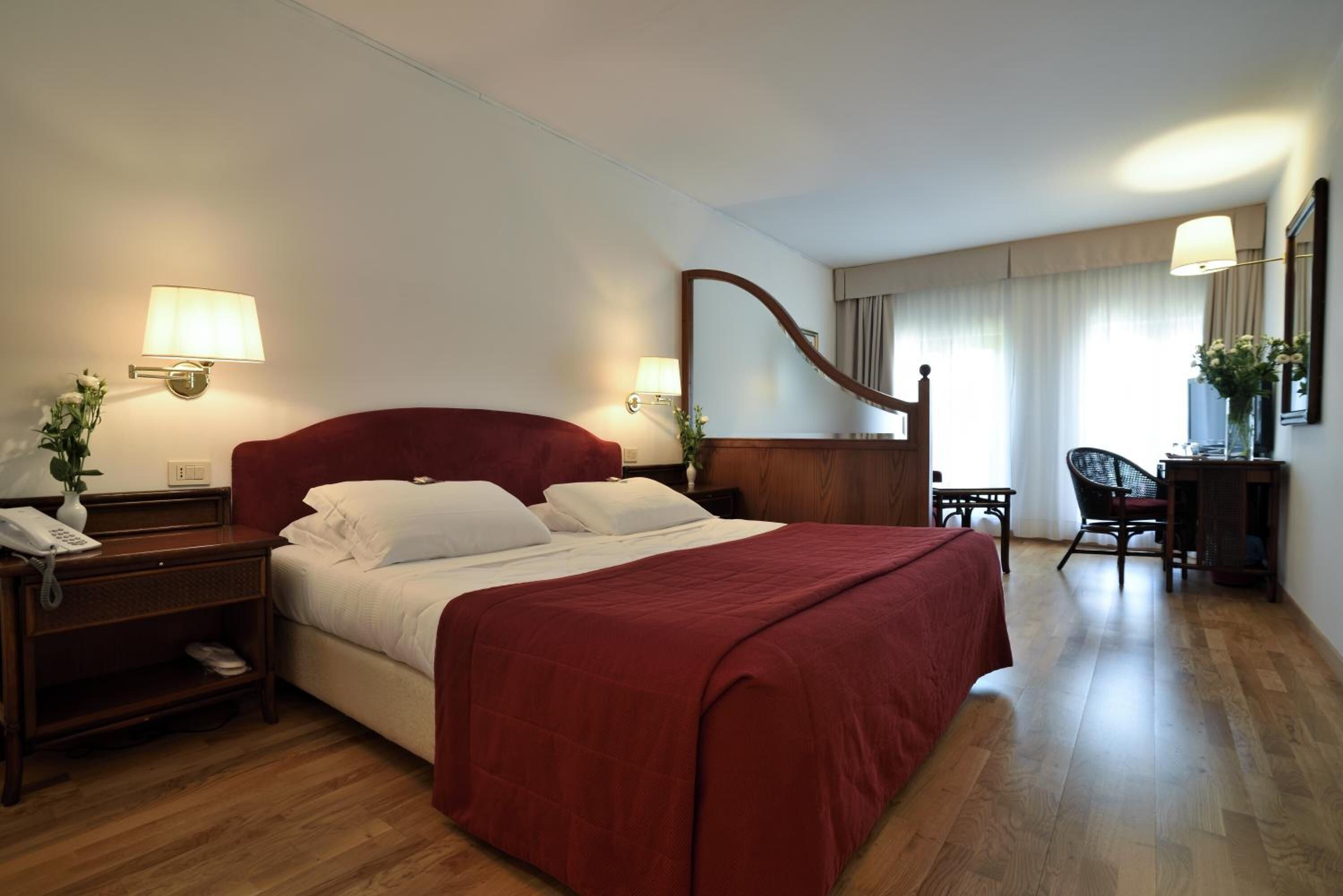 Habitación de hotel con una cama grande, dos mesitas de noche con lámparas, un escritorio de madera, una silla y un espejo.