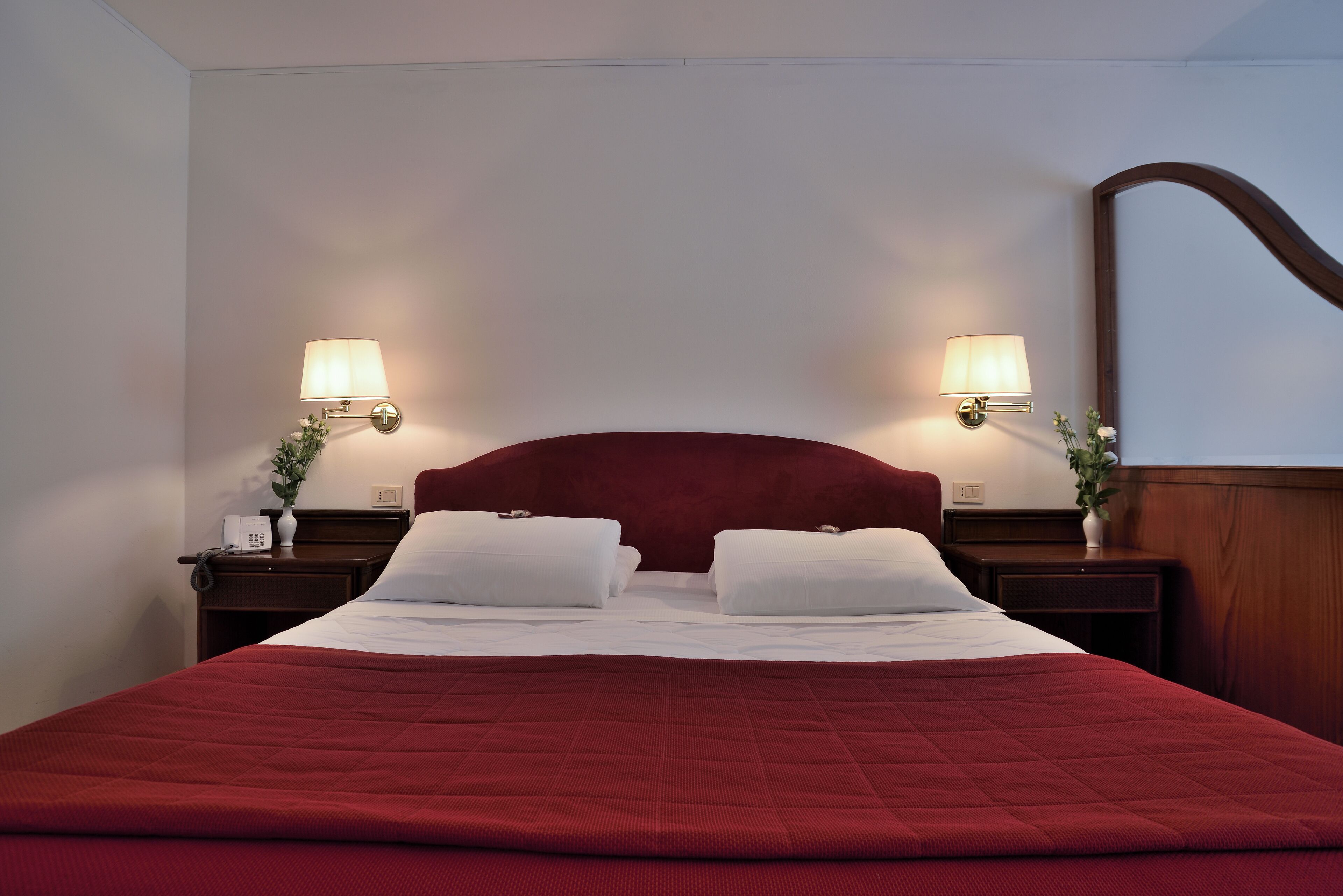 Una habitación de hotel con una cama grande, dos mesitas de noche con lámparas y un cabecero de madera.