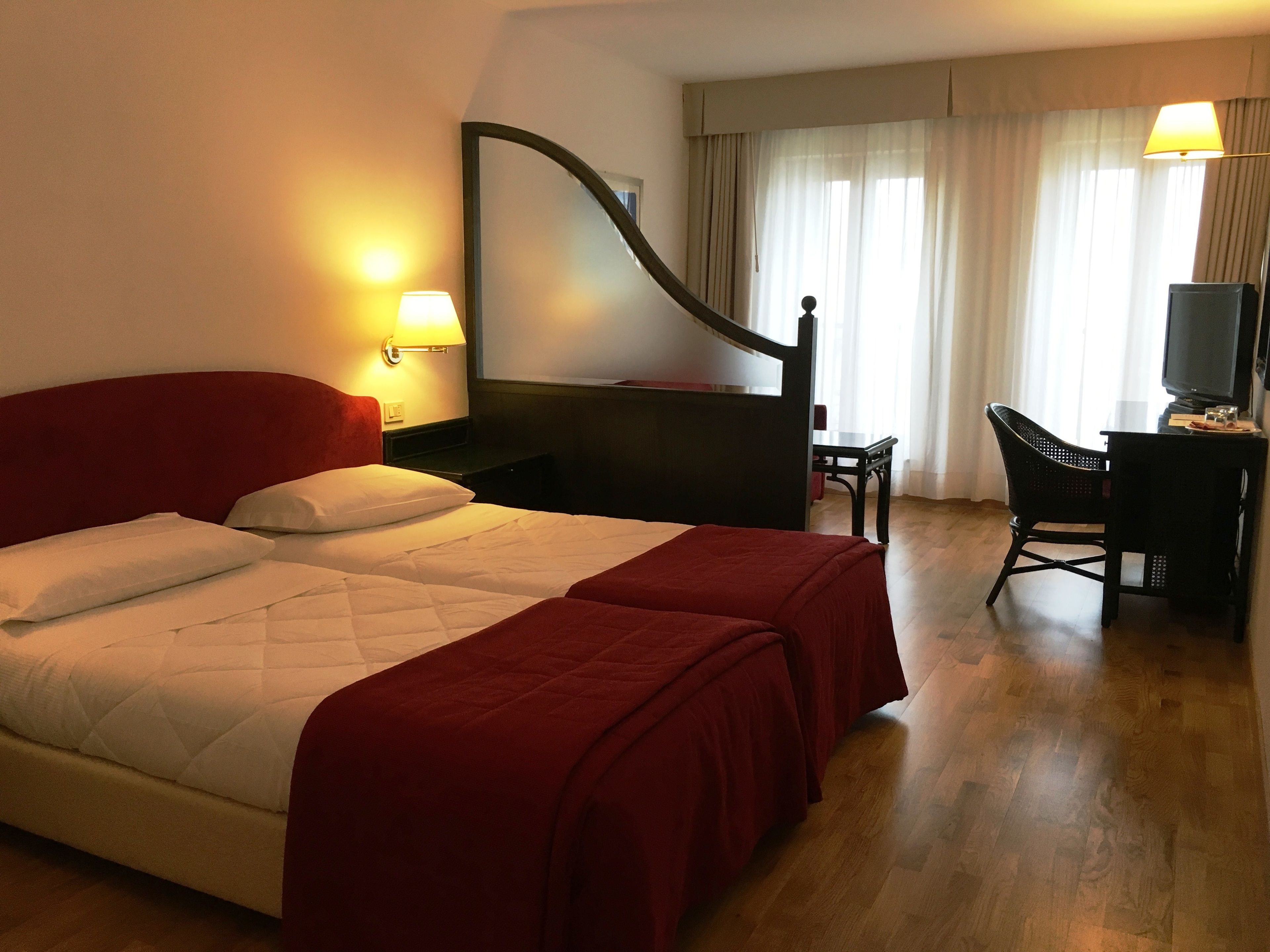 Habitación de hotel con cama doble, dos mesitas de noche, un escritorio con silla, televisor y un espejo grande.