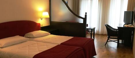 Habitación de hotel con cama doble, dos mesitas de noche, un escritorio con silla, televisor y un espejo grande.