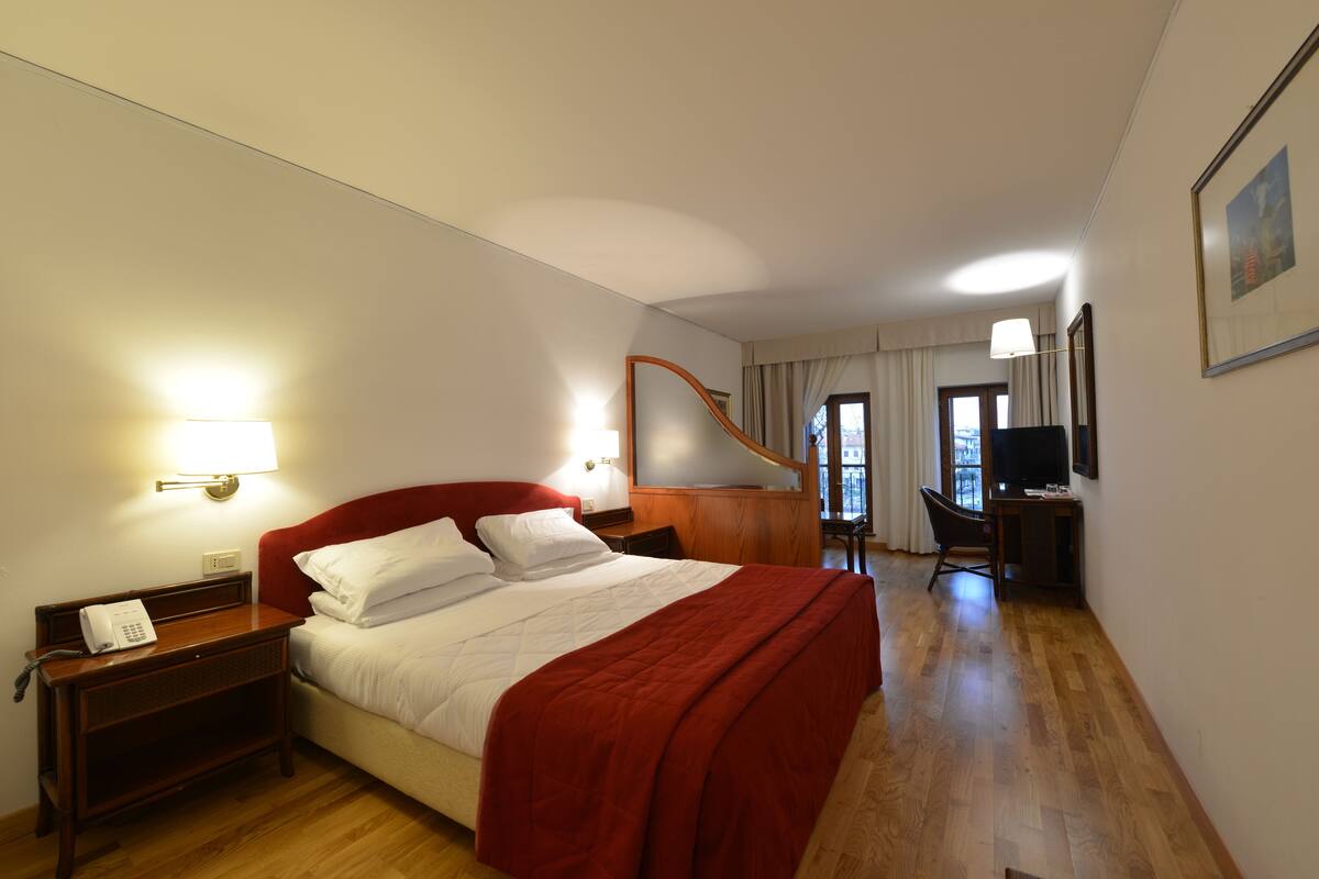 A hotel room with a bed, a desk, a chair, a TV, and a lamp.