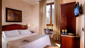 Habitación de hotel con una cama grande, un televisor de pantalla plana en la pared, un escritorio de madera con una silla y una ventana con cortinas.