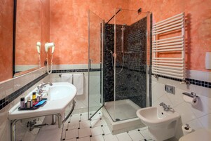 Een moderne badkamer met een glazen douchecabine, een bidet, een wastafel met toiletartikelen en een handdoekrek.
