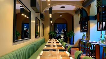 Un restaurante con mesas largas compartidas, asientos tapizados en tonos verdes y lámparas colgantes.