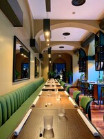 Un ristorante con lunghe tavolate condivise, comode panche imbottite di verde e lampadari pendenti.
