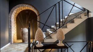 Una escalera moderna con barandilla metálica de diseño geométrico, un arco de ladrillo y dos jarrones decorativos sobre una consola.