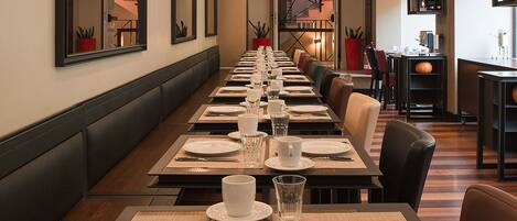 A long dining table set with multiple chairs, a red potted plant, and a staircase in the background.