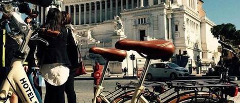 A bicycle with a seat labeled "HOTEL SAN FRANCESCO" parked in front of a classical building with columns and statues.