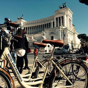 A bicycle with a seat labeled "HOTEL SAN FRANCESCO" parked in front of a classical building with columns and statues. - Hotel San Francesco (Rome)
