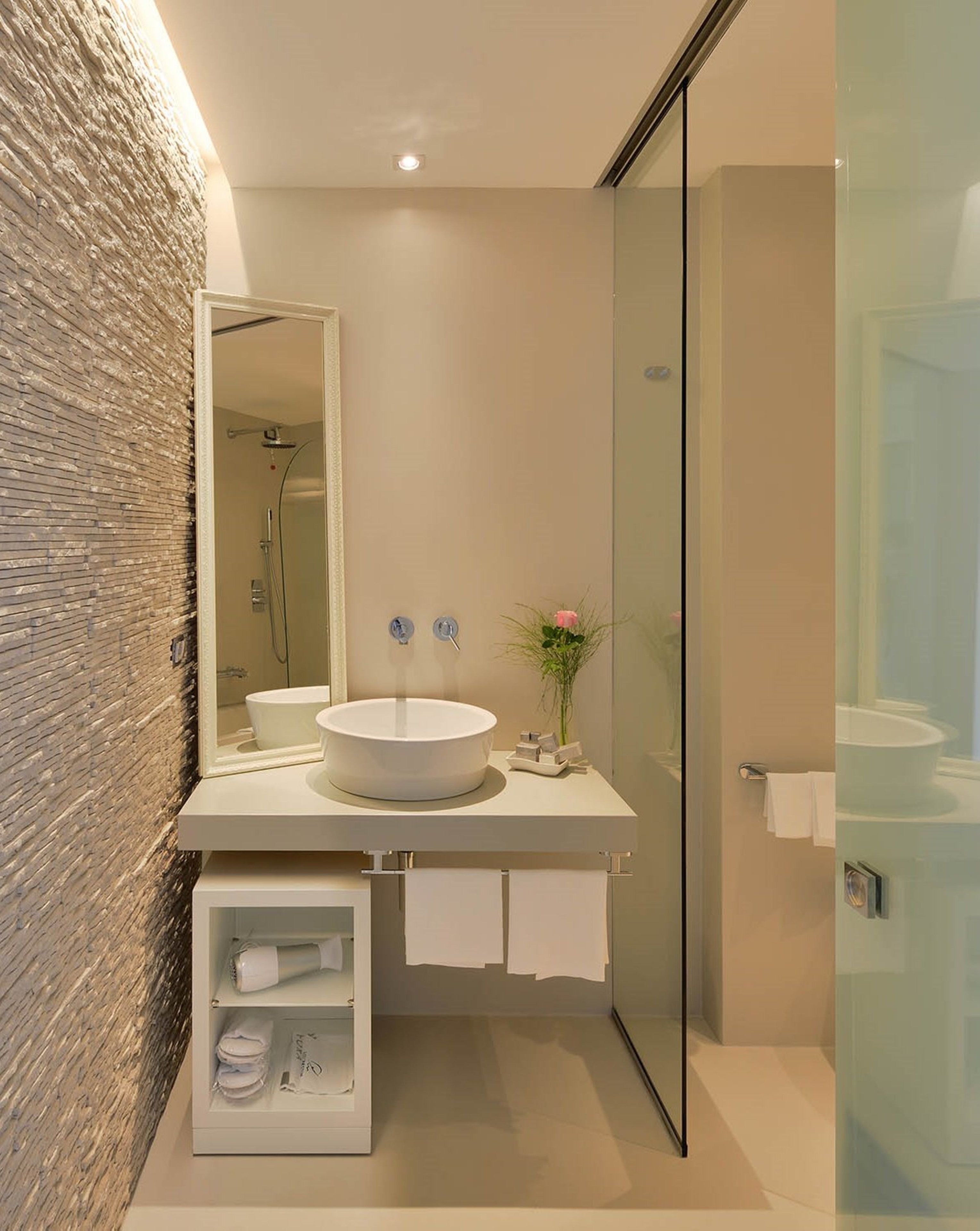 A modern bathroom with a large mirror, a round sink, and a glass shower enclosure.