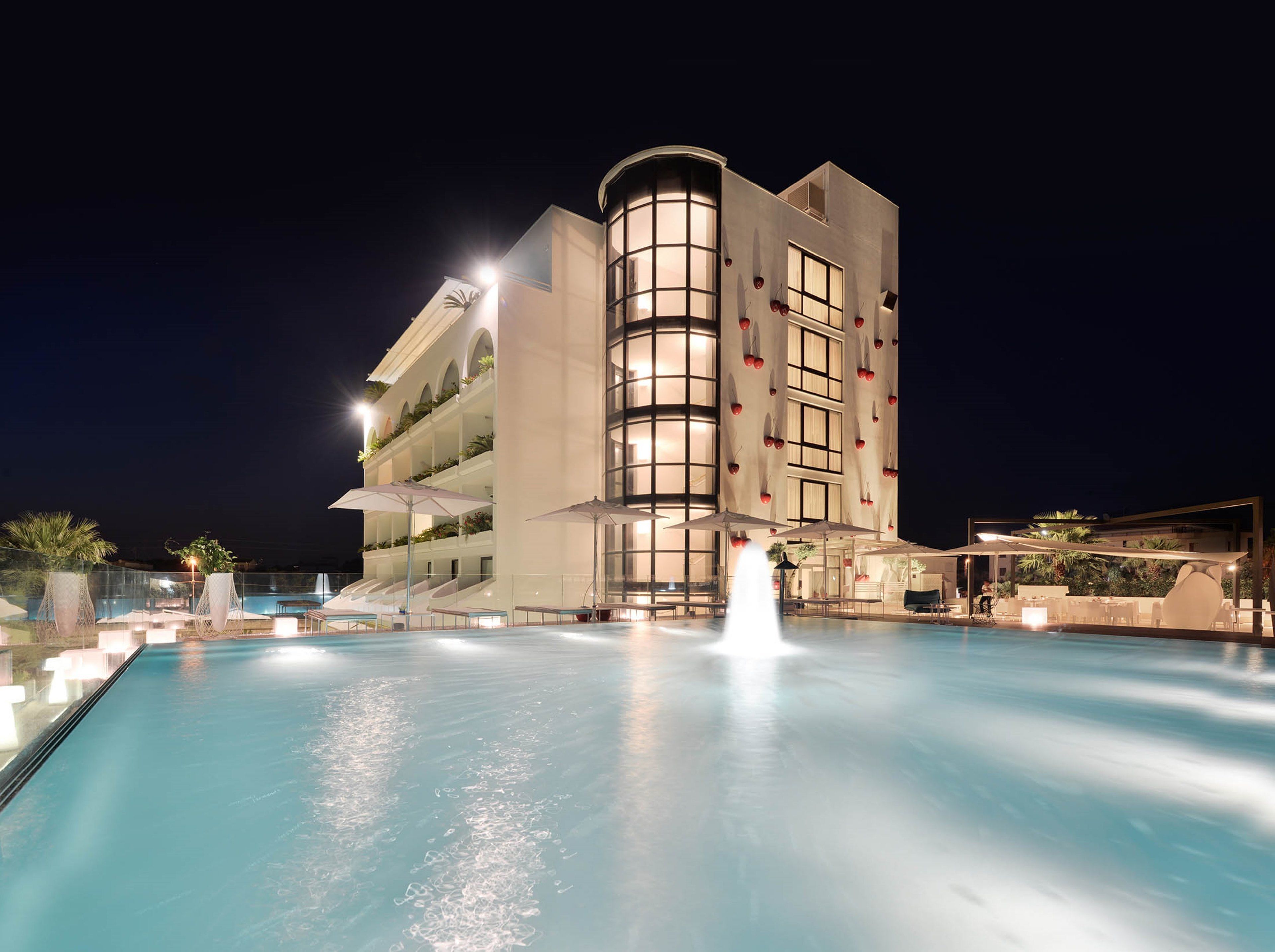 A hotel with a pool, outdoor seating, and a fountain.