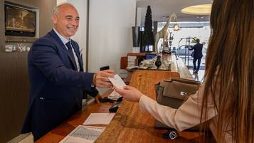Una reception d'albergo con un uomo che porge una tessera a una donna.
