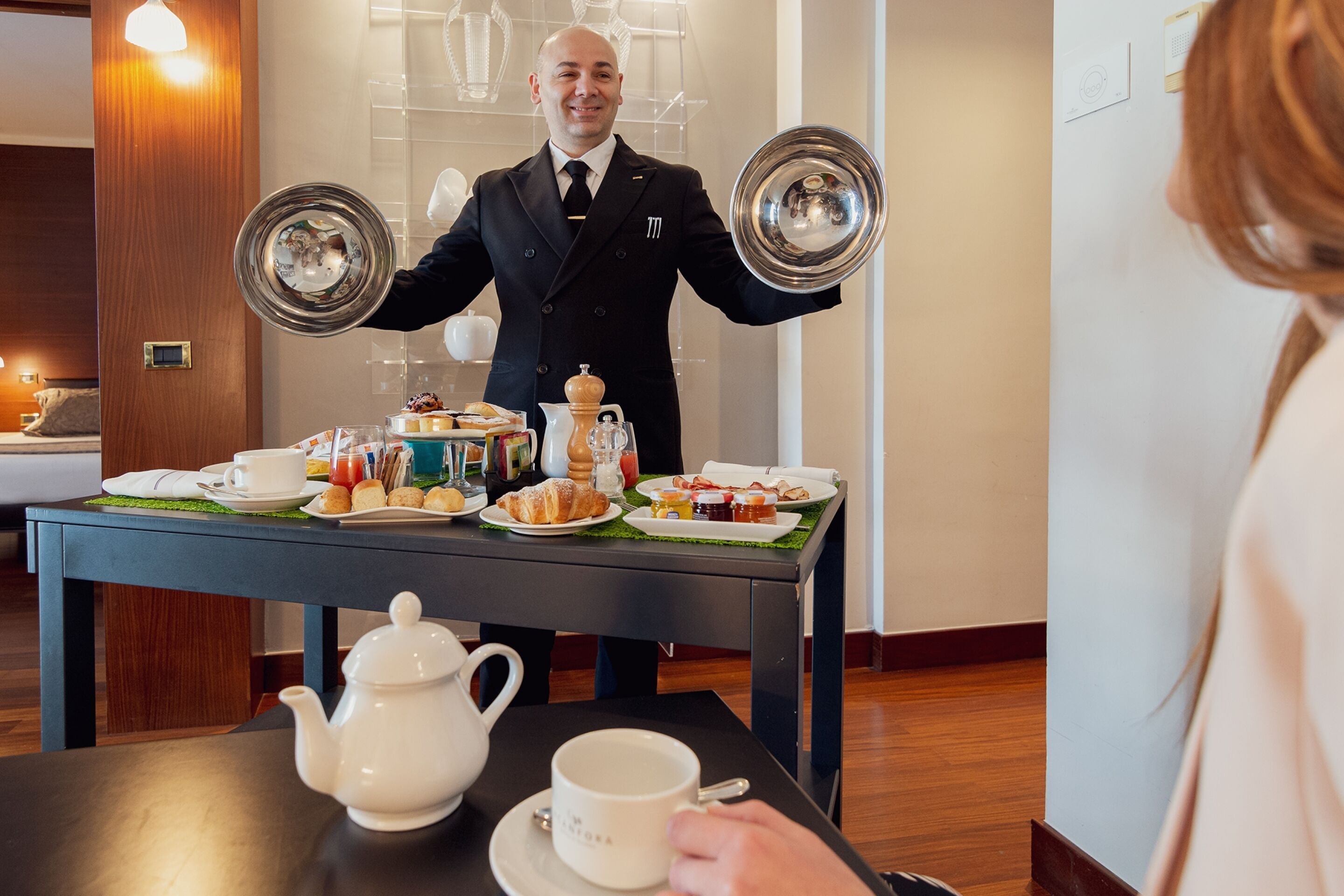 Une chambre d’hôtel avec une table à manger dressée pour le petit-déjeuner, comprenant des viennoiseries, une théière et une tasse.