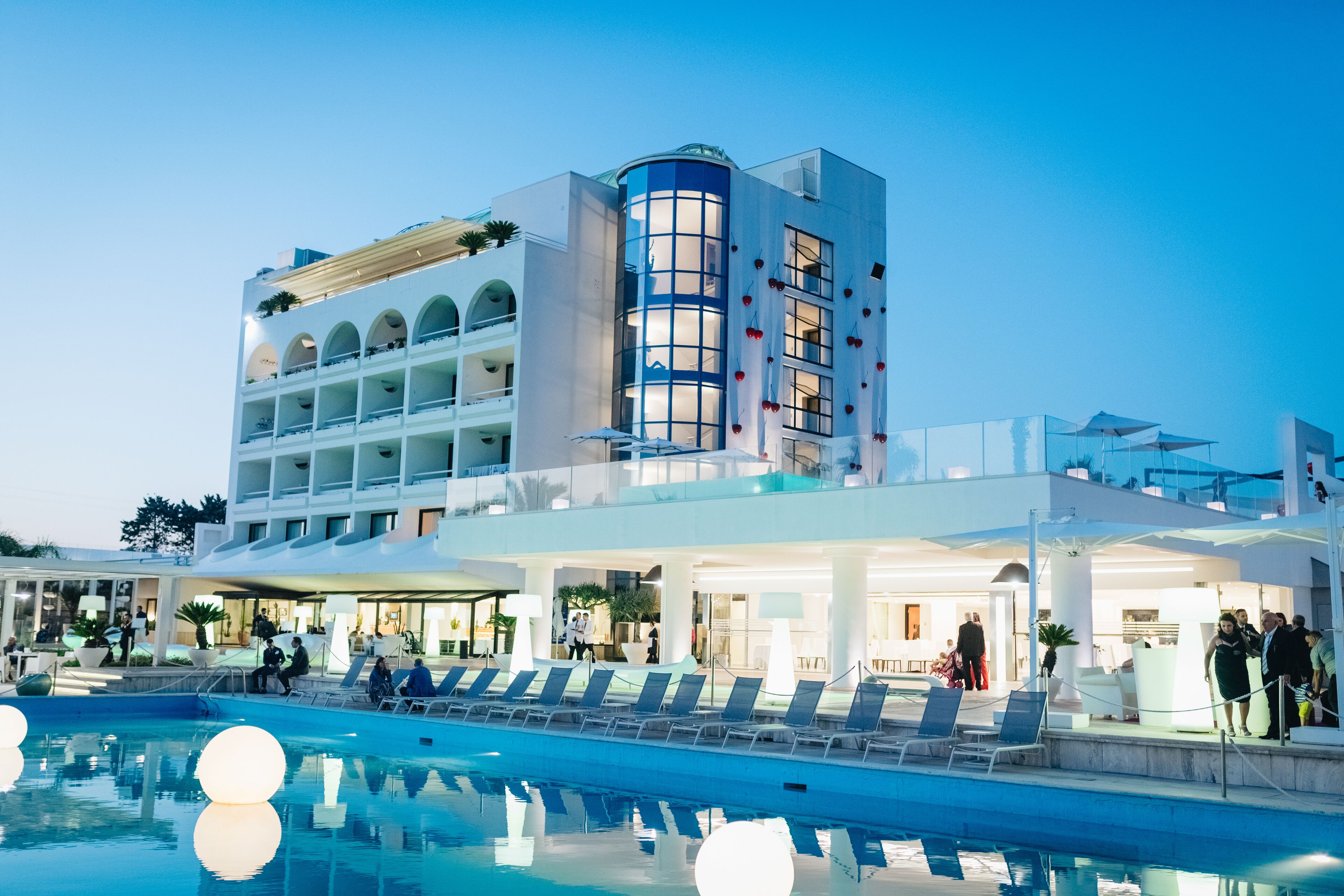 A modern hotel with a pool, multiple balconies, and a well-lit lobby area.