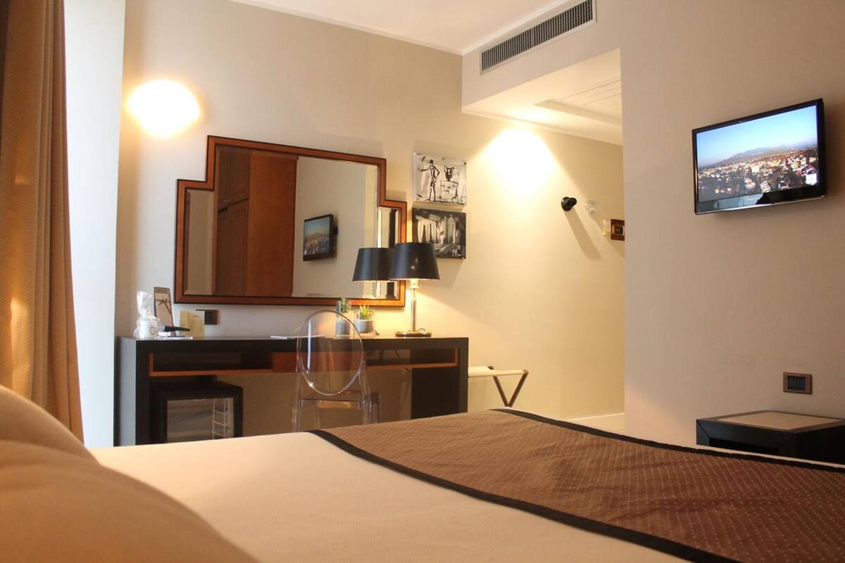 Una habitación de hotel con cama, escritorio, silla, televisor y un espejo grande.