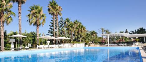 A swimming pool with lounge chairs and umbrellas, surrounded by palm trees.